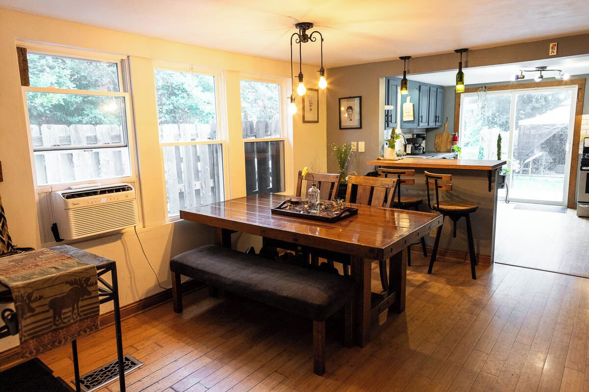 A dining area with a wooden table, benches, and a kitchen in the background.