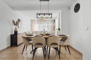 A dining area with a rectangular table, six chairs, a hanging light fixture, and a clock on the wall.