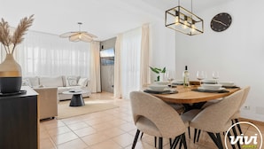Una sala de estar moderna con un sofá, una mesa de comedor para dos personas y un televisor montado en la pared.