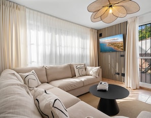Uma sala de estar moderna com um amplo sofá de canto, uma mesa de centro redonda preta e uma televisão fixada na parede com vista panorâmica.
