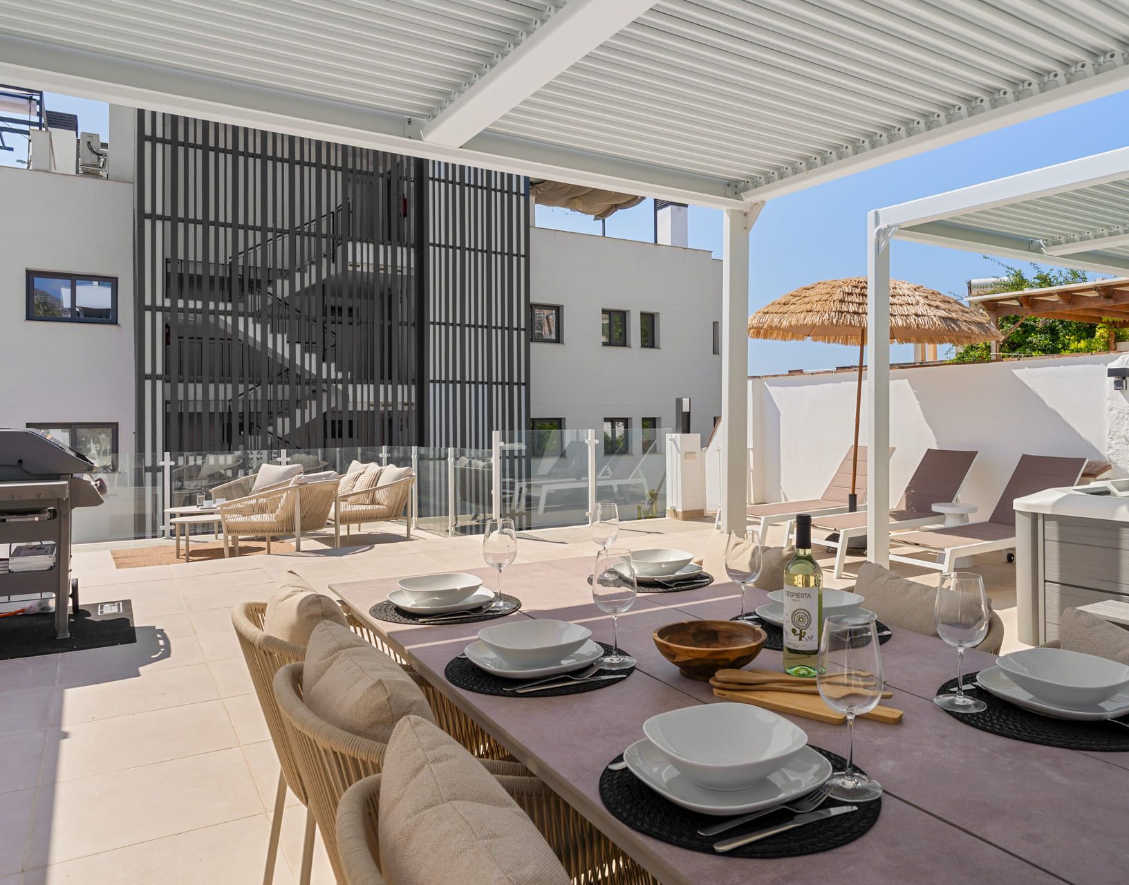 Un área de comedor al aire libre moderna con terraza, mobiliario de mimbre y una mesa lista para dos.
