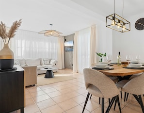 Uma sala de estar moderna com um sofá, uma mesa de jantar posta para dois e uma TV na parede.