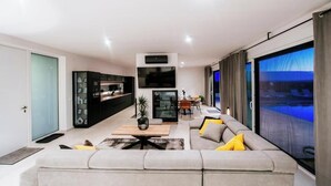 A modern living room with a large sofa, a coffee table, and a TV. There is a dining area with a table and chairs. The room has a large window with curtains. - Perfect villa Stressless with beautiful pool in charming Smoković (Smoković)