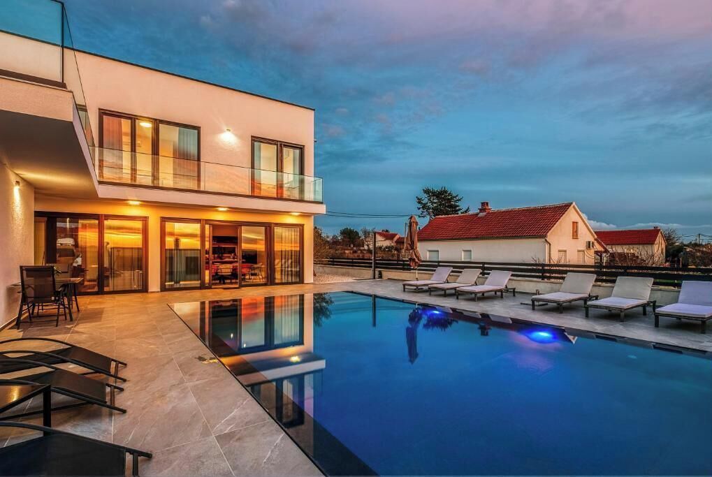 Une maison moderne à deux étages, dotée d’une piscine, de chaises longues et d’un espace repas.