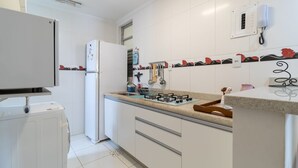 Moderni keittiö, jossa on valkoiset kaapit, kaasuliesi, jääkaappi ja sisäänrakennettu mikroaaltouuni.