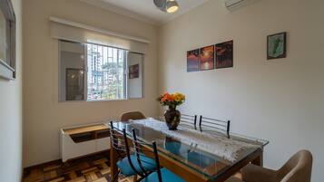 A dining area with a glass table, blue chairs, a vase with flowers, and artwork on the wall.