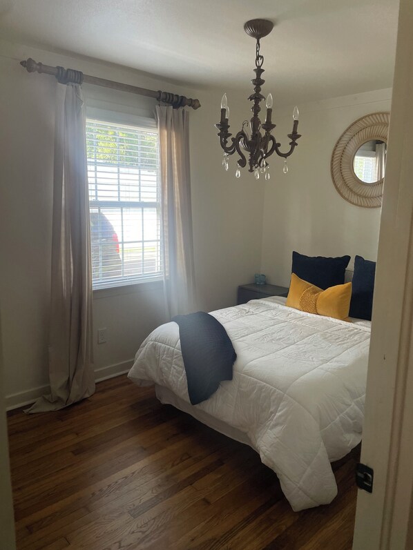 Un dormitorio con cama, candelabro, ventana con cortinas y un espejo redondo en la pared.