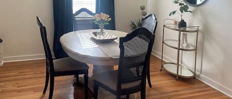 A dining area with a round table, four chairs, a chandelier, a mirror, and a plant.