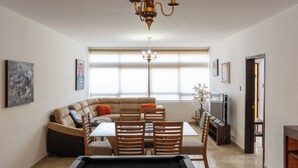 A living room with a sofa, dining table, chairs, a chandelier, a TV, and artwork on the walls. - Vive Oaxaca: Secure Parking and Space for Groups (Oaxaca de Juárez)