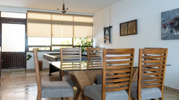 A dining area with a glass table, wooden chairs, and a chandelier. - Vive Oaxaca: Secure Parking and Space for Groups (Oaxaca de Juárez)