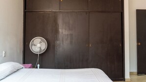 A bedroom with a bed, a white fan, and a dark wardrobe. - Vive Oaxaca: Secure Parking and Space for Groups (Oaxaca de Juárez)