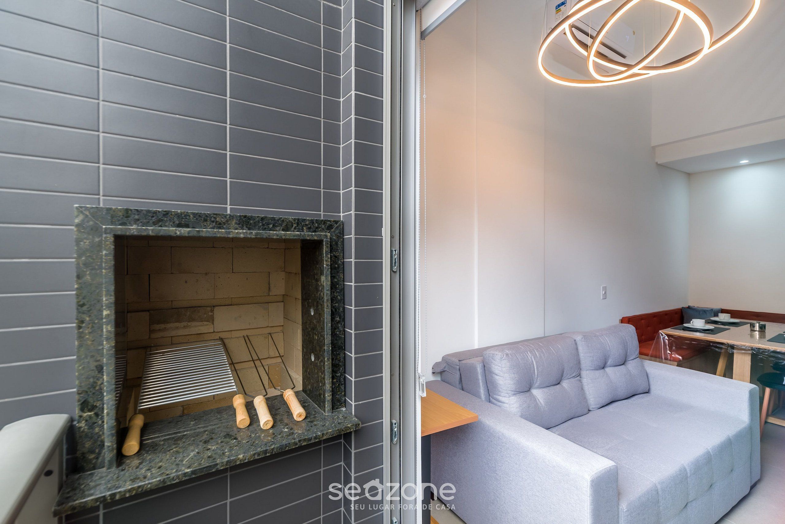 A modern interior with a grey tiled wall, a fireplace with a metal grate, and a grey sofa in a corner.