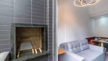 A modern interior with a grey tiled wall, a fireplace with a metal grate, and a grey sofa in a corner.