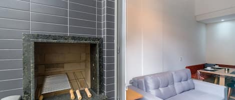 Un intérieur moderne avec un mur recouvert de carreaux gris, une cheminée dotée d’un foyer en métal et un canapé gris placé dans un coin.