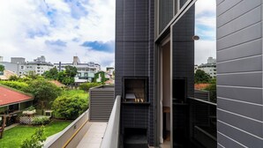 A modern building with a dark facade, a small outdoor area with greenery, and a view of other buildings in the background. - Apartment With Barbecue 280m From Ert0210 Beach (Florianópolis)
