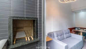 A modern kitchen with a built-in fireplace, grey tiles, and a grey sofa in a living area. - Apartment With Barbecue 280m From Ert0210 Beach (Florianópolis)