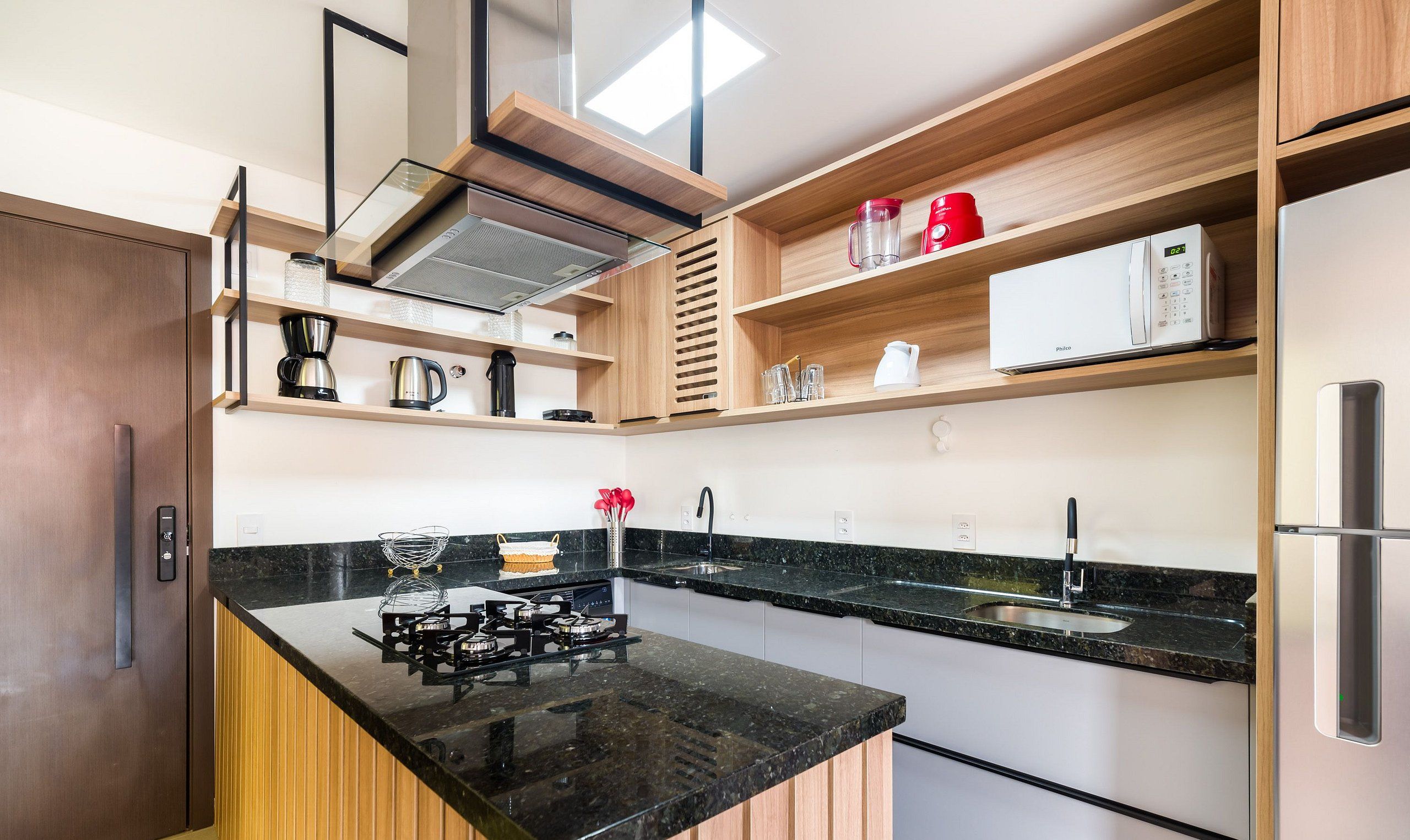Een moderne keuken met een zwart granieten aanrecht, roestvrijstalen apparatuur en houten planken.