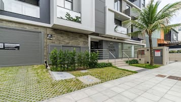 Un edificio moderno con entrada protegida por una reja, una escalera que conduce a la entrada, y un pequeño jardín con césped y arbustos.