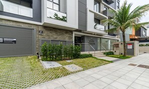 Un bâtiment moderne doté d’une entrée sécurisée par un portail, d’un escalier menant à l’entrée et d’un petit jardin avec de la pelouse et des arbustes.
