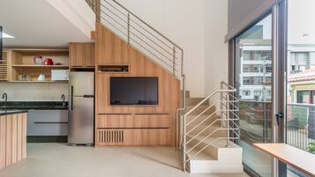 A modern kitchen with wooden cabinets, a built-in TV, and a stainless steel refrigerator.