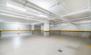 A spacious parking garage with white ceilings, fluorescent lighting, and yellow safety lines on the floor. - Apartment With Barbecue 280m From Ert0210 Beach (Florianópolis)