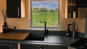 Eine Küche mit schwarzer Arbeitsplatte, einem Fenster mit Blick auf ein grünes Feld und einem schwarzen Schrank über der Spüle.