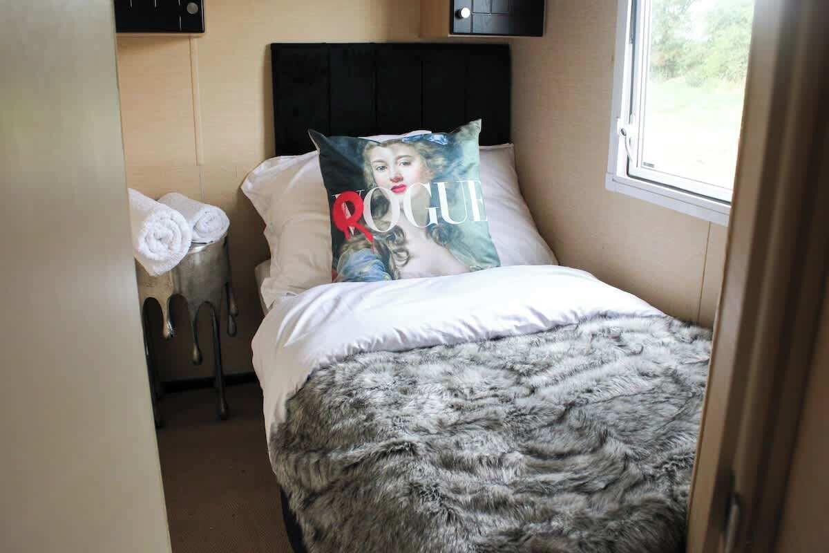 Una camera da letto con un letto, un cuscino con una copertina di rivista, una finestra e un portasciugamani.