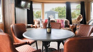 Ein gemütliches Interieur mit Ledersesseln um einen runden Tisch, einer Weinflasche und Blick auf ein Haus durch große Fenster.