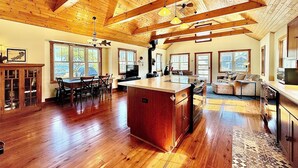 A spacious kitchen with wooden beams, a large island, and a dining area with chairs and a table. - Lake Delavan Hideaway - Carl’s Cottage - Water View Bliss, Dock & Cozy Fireplace (Delavan)