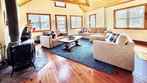 A spacious living room with wooden floors, a fireplace, and large windows. - Lake Delavan Hideaway - Carl’s Cottage - Water View Bliss, Dock & Cozy Fireplace (Delavan)