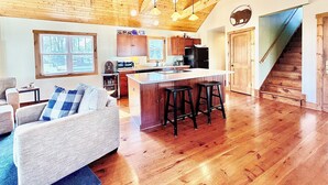 A spacious living area with a wooden ceiling, a kitchen with a central island, and a staircase leading to another level. - Lake Delavan Hideaway - Carl’s Cottage - Water View Bliss, Dock & Cozy Fireplace (Delavan)
