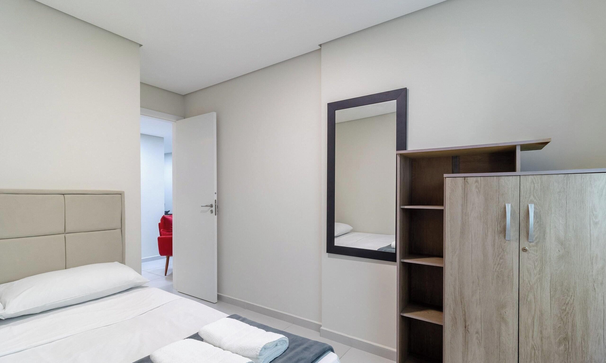 A modern hotel room with a bed, a wardrobe, and a mirror.