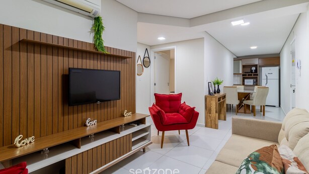 Ein modernes Wohnzimmer mit Flachbildfernseher, einem roten Sessel und einem beigen Sofa.