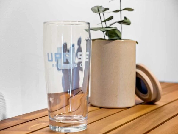 A clear glass with a reflection of a cityscape, placed on a wooden surface next to a cylindrical container with a plant.