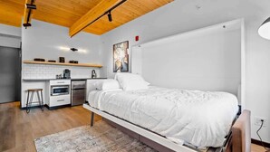 A modern bedroom with a loft bed, a kitchenette, and a wooden ceiling. - Uprise 2 Bridgewater Lofts (Spokane)