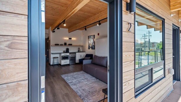 A modern interior with a wooden ceiling, a kitchen area, and a seating area with a sofa and rug. - Uprise 2 Bridgewater Lofts (Spokane)