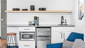 A modern kitchen with white subway tiles, stainless steel appliances, a coffee machine, and a blue sofa in the living area. - Uprise 2 Bridgewater Lofts (Spokane)