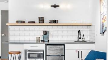 Uma cozinha moderna com azulejos brancos tipo metrô, eletrodomésticos de aço inoxidável, uma cafeteira e um sofá azul na sala de estar.