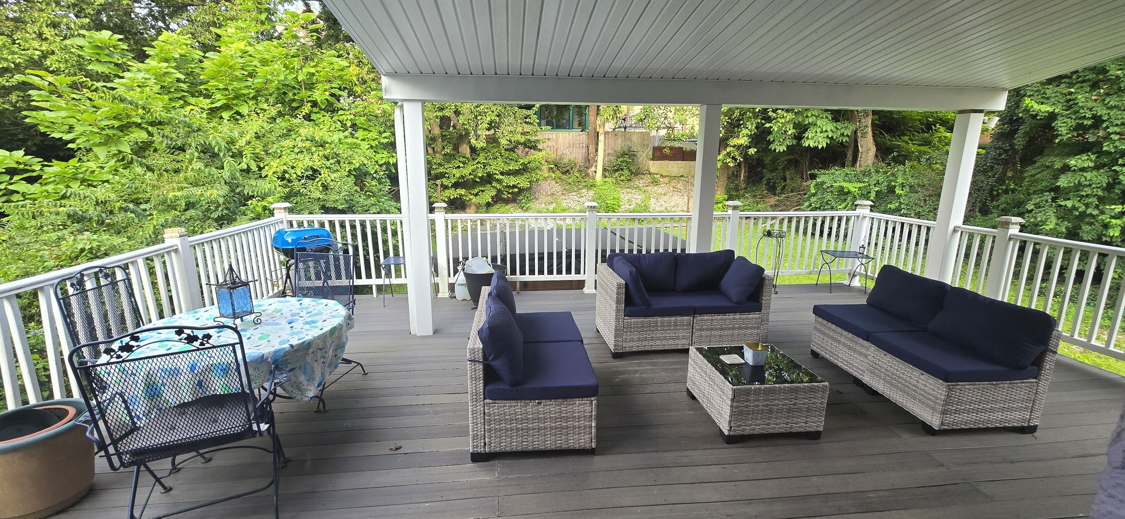 A covered outdoor deck with wicker furniture, a table, and a grill.
