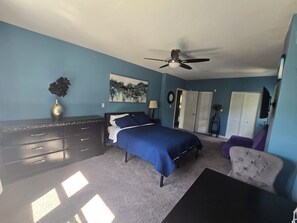 Ein Schlafzimmer mit Bett, Kommode, Deckenventilator und einem Sessel.