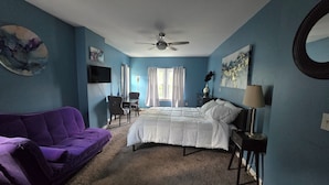 A bedroom with a bed, a purple sofa, a desk, a chair, a ceiling fan, and artwork on the walls. - Charming 3-bedroom house in enchanting Cincinnati with AC Heat washer and dryer (Cincinnati)