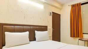 Ein Hotelzimmer mit einem großen Bett, einem Holzkopfstück, einem kleinen Tisch und einem Fenster mit Vorhängen.