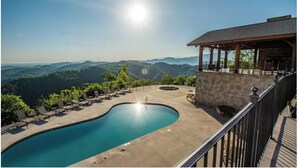 A pool with a view of mountains, a covered seating area, and a stone wall. - Luxury-8BR-Lodge-Game Room-Theater&MountainViews (Sevierville)