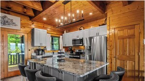 A modern kitchen with granite countertops, stainless steel appliances, and a central island with bar stools. - Luxury-8BR-Lodge-Game Room-Theater&MountainViews (Sevierville)