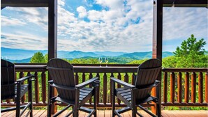 A wooden deck with two Adirondack chairs and a glass of wine, overlooking a mountainous landscape. - Luxury-8BR-Lodge-Game Room-Theater&MountainViews (Sevierville)