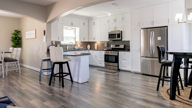 A modern kitchen with white cabinetry, stainless steel appliances, and a central island with bar stools. - Tranquil 3-bedroom house with dock in Kemah (Kemah)
