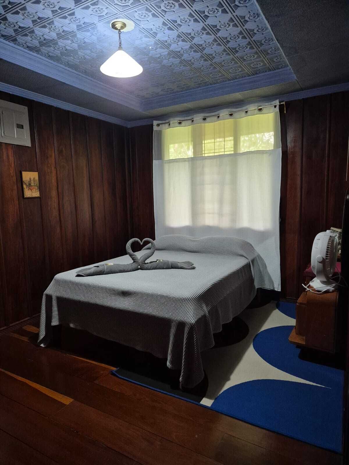 Une chambre à coucher avec un lit, un ventilateur de plafond et une fenêtre avec des rideaux.