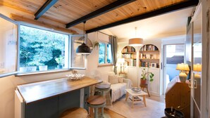 Eine gemütliche Küche mit Holzboden, ein Essbereich mit Tisch und Stühlen und ein Ausblick ins Freie durch ein großes Fenster.