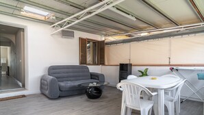 A room with a grey sofa, a round glass coffee table, a white table with chairs, a window with wooden shutters, and a speaker. - La Corte Rurale Apartment with Hot Tub (Lucca)