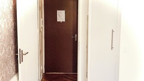 Un couloir doté d’un plancher en bois et de portes blanches, qui mène à une pièce dont la porte est sombre et sur laquelle est affichée une annonce.